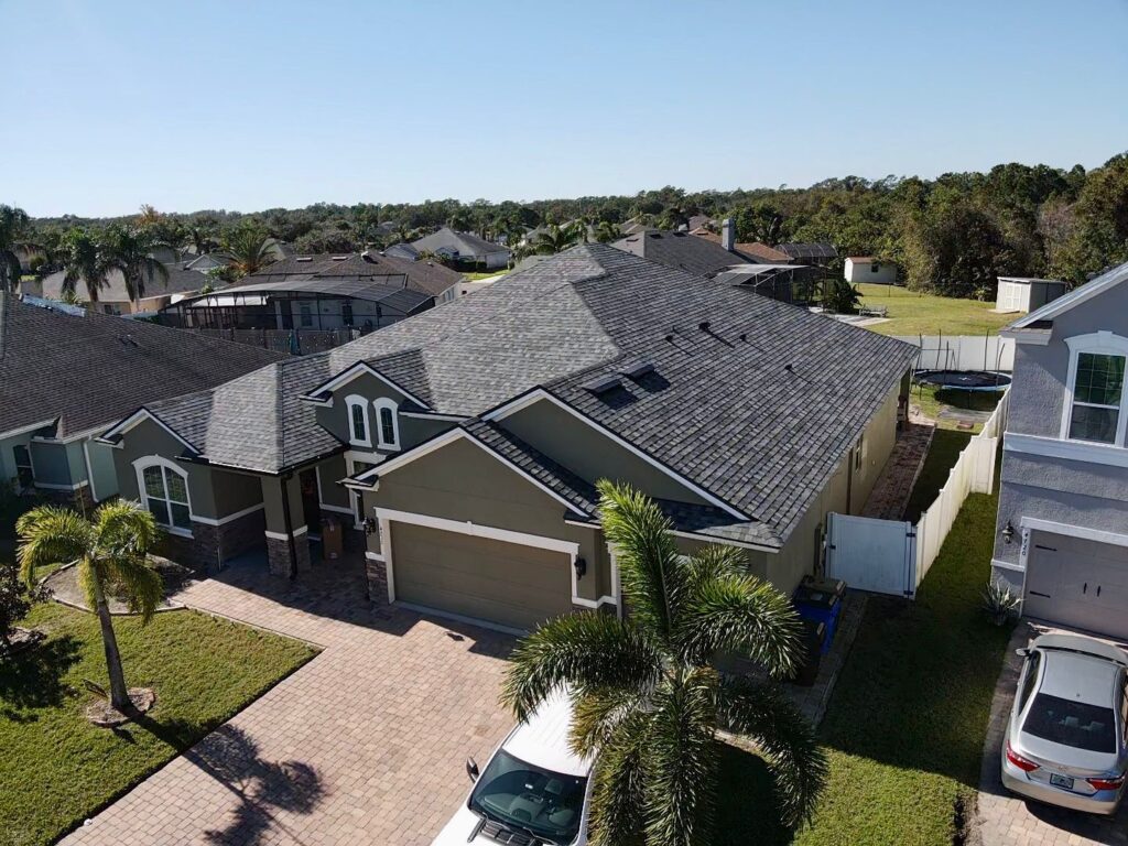 Aerial view of a suburban house with a gray roof, driveway, and palm trees in a residential neighborhood in Florida, where understanding roof permit requirements is essential for any renovation.