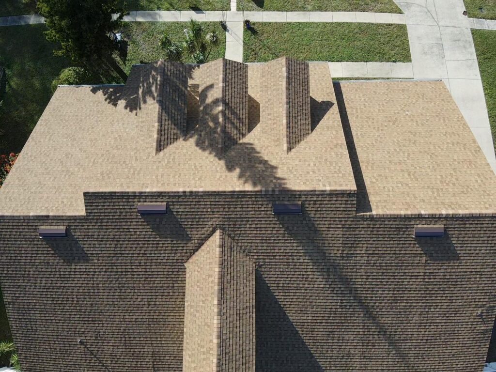 Aerial view of a brown shingle roof with chimneys, surrounded by grass and intersecting concrete paths, highlighting the importance of understanding roof permit requirements in Florida.