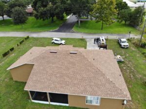Aerial view of a brown-roofed house, expertly crafted by a roofing contractor in Lakeland, with two vehicles parked in the driveway, surrounded by green lawns and trees.