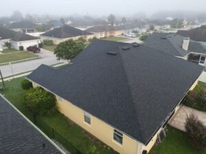 Aerial view of a suburban neighborhood with houses featuring dark roofs, maintained by a Lakeland roofing company, under a foggy sky and well-kept lawns.