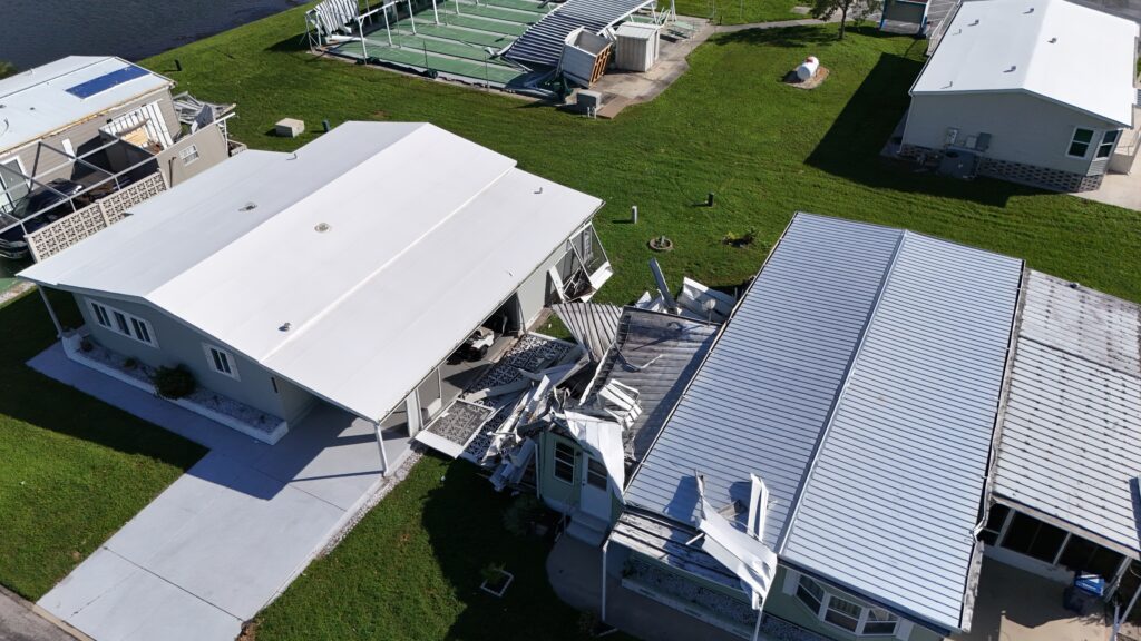 An aerial view reveals two houses with roof damage and debris scattered on the green lawns, reminiscent of scenes often found in mobile home communities in need of roof repair.